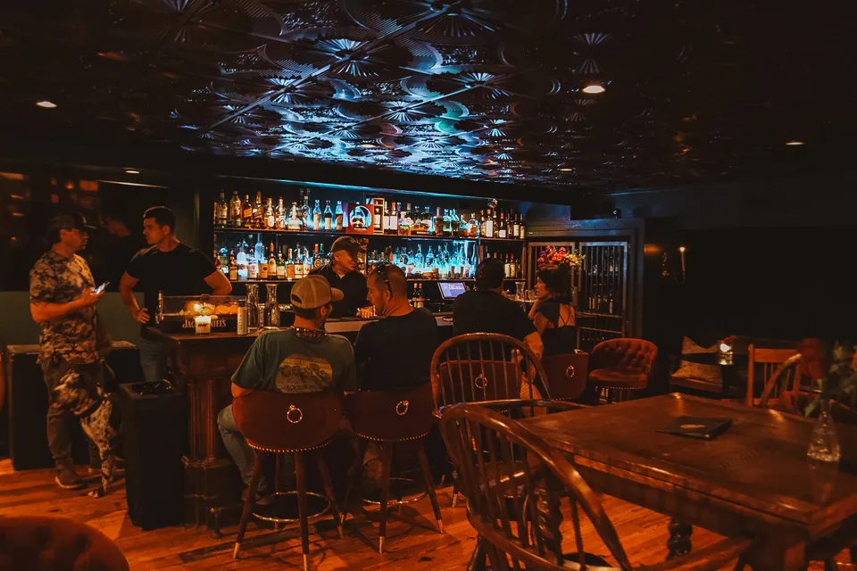 The backbar lit blue under the pressed-tin ceiling, every stool taken, the long tables waiting.