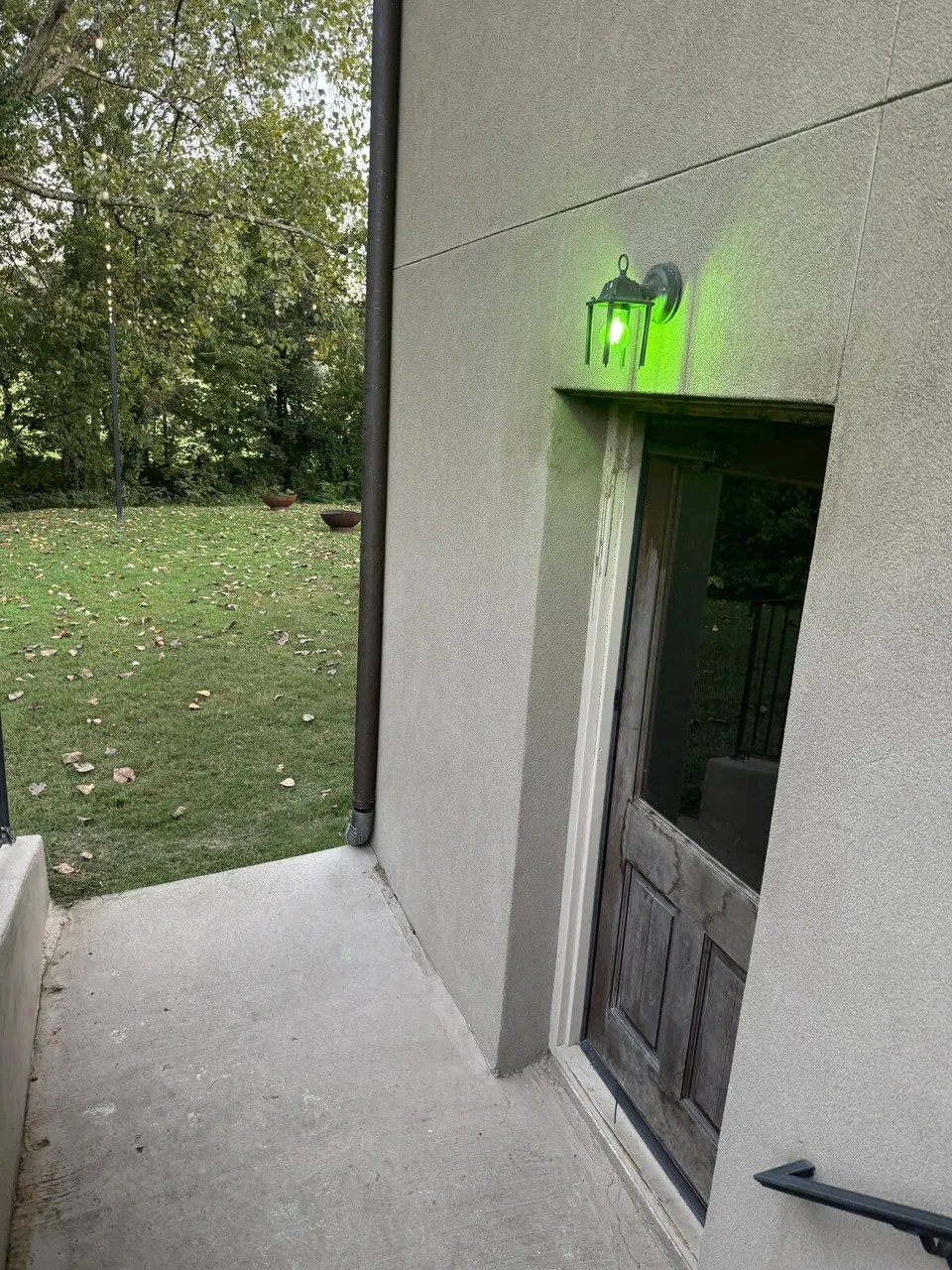 The weathered wood basement door with a green lantern glowing above it, at the bottom of the outside stairs.
