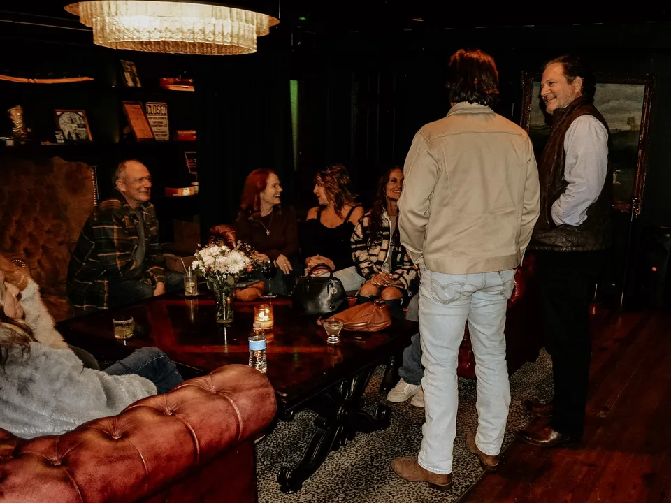 Guests standing and sitting around the lounge’s low table under the chandelier, mid-conversation.